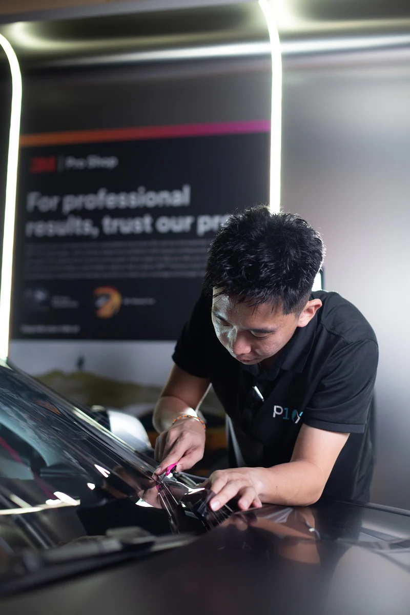 A technician working at the edge of windscreen film during installation.